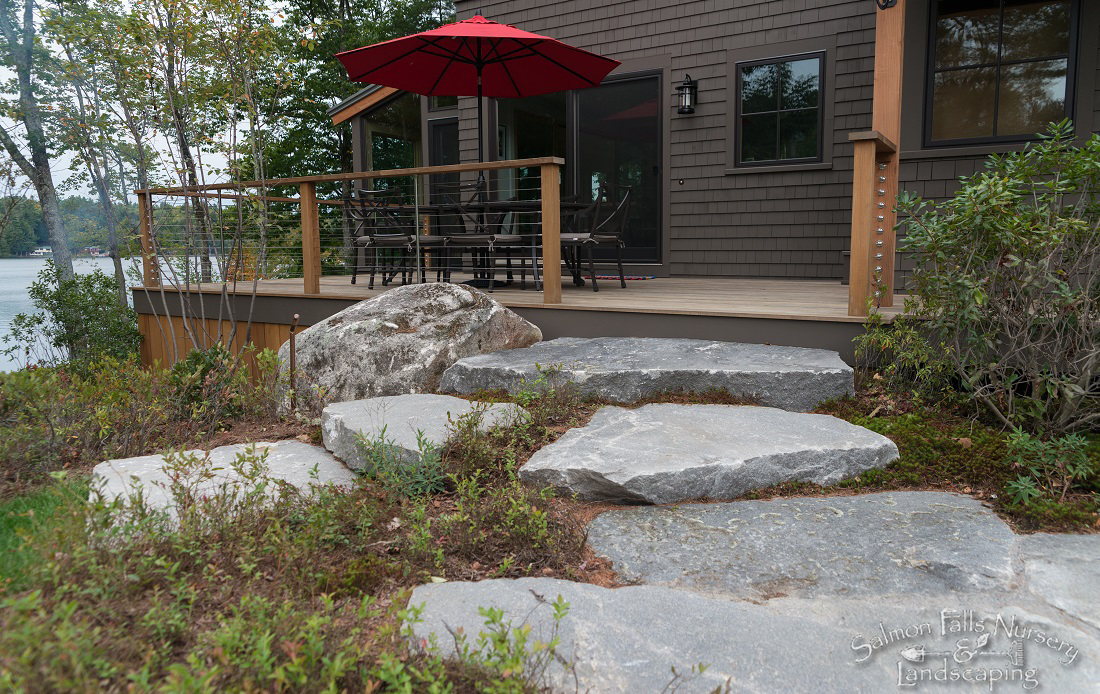Natural stone steps leading up to a lakeside deck with a red umbrella